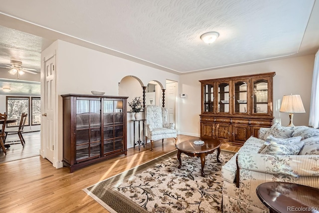 living room featuring a textured ceiling, light wood-type flooring, and ceiling fan