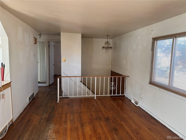 unfurnished room featuring dark wood-type flooring and a notable chandelier