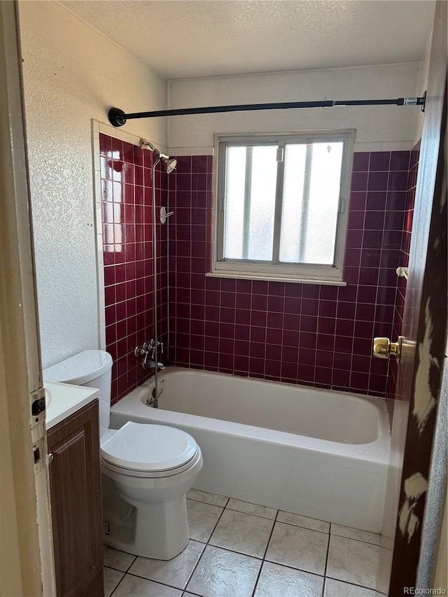 full bathroom with a textured ceiling, vanity, tiled shower / bath combo, tile patterned flooring, and toilet