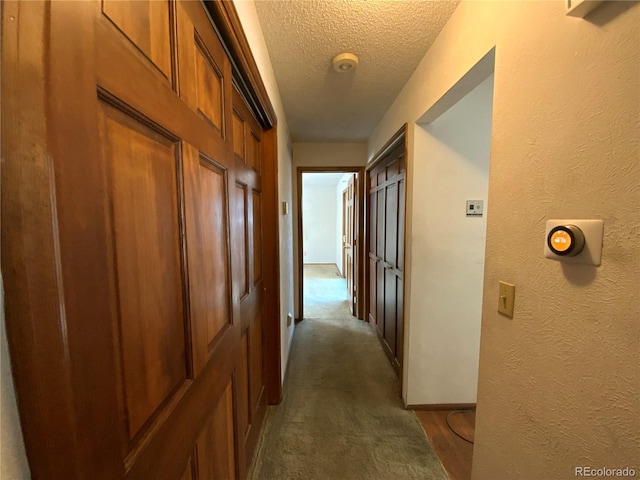 hall featuring dark carpet and a textured ceiling