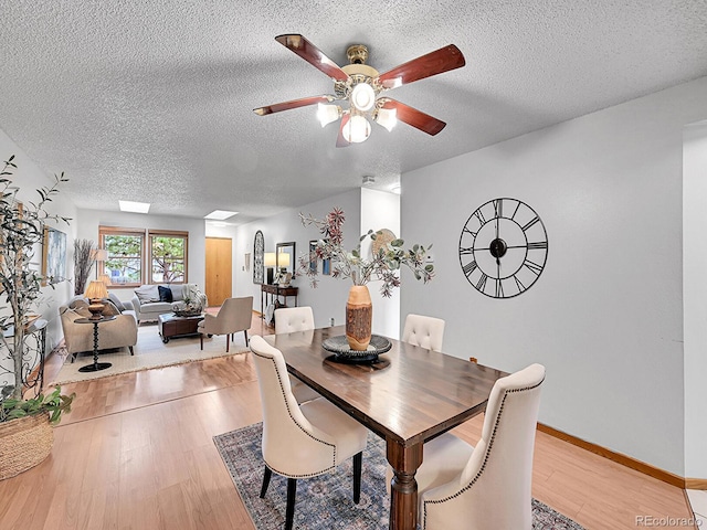 dining area with a textured ceiling, baseboards, a ceiling fan, and light wood-style floors