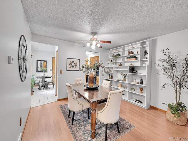 dining room featuring light wood finished floors, baseboards, a ceiling fan, and a textured ceiling