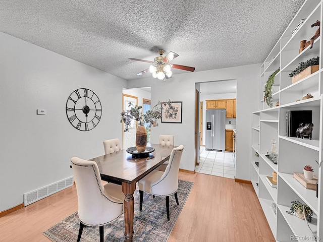 dining room featuring visible vents, ceiling fan, light wood-style flooring, and a textured ceiling