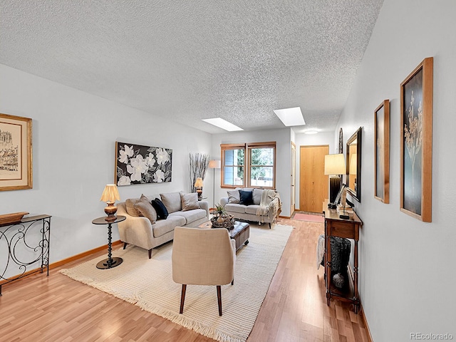 living area featuring a textured ceiling, a skylight, light wood-style flooring, and baseboards