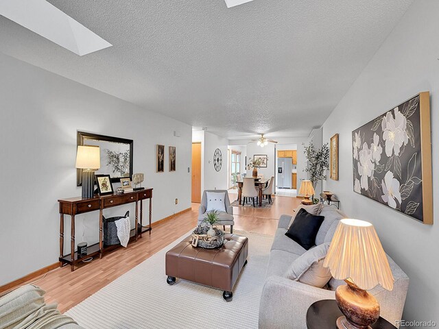 living area featuring a skylight, ceiling fan, light wood-style flooring, and a textured ceiling