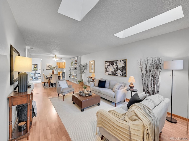 living room featuring light wood-type flooring, a skylight, a textured ceiling, and a ceiling fan