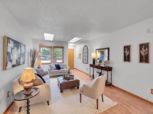 living room with a skylight, a textured ceiling, baseboards, and light wood-style floors