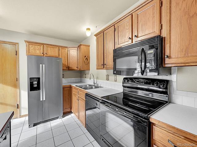 kitchen featuring brown cabinetry, light countertops, black appliances, a sink, and light tile patterned flooring