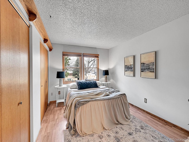 bedroom featuring light wood-type flooring, a textured ceiling, and baseboards