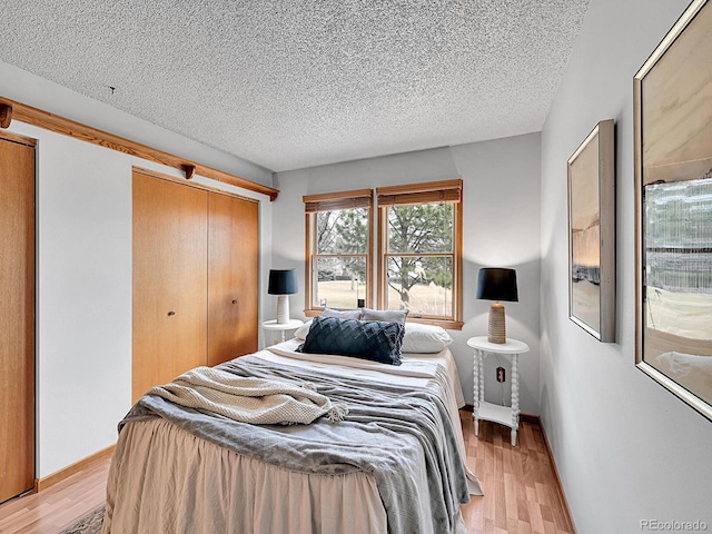 bedroom with light wood-type flooring, a closet, baseboards, and a textured ceiling