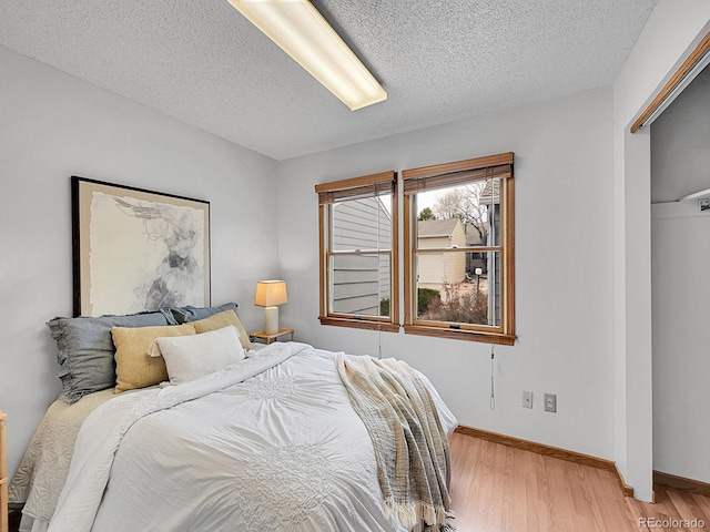 bedroom with a textured ceiling, light wood finished floors, and baseboards