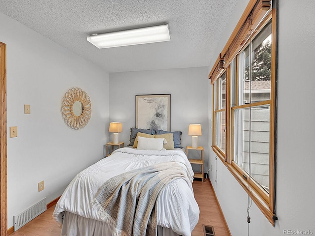 bedroom featuring light wood-style floors, baseboards, visible vents, and a textured ceiling