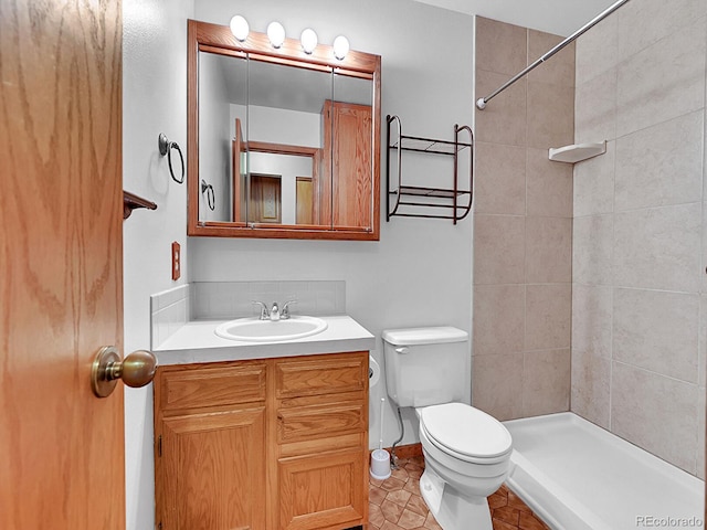 bathroom featuring toilet, a tile shower, vanity, baseboards, and tile patterned floors