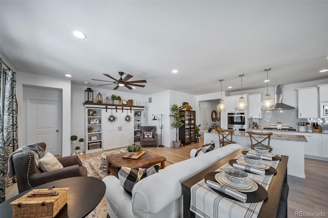 living room featuring light wood-type flooring, a ceiling fan, and recessed lighting