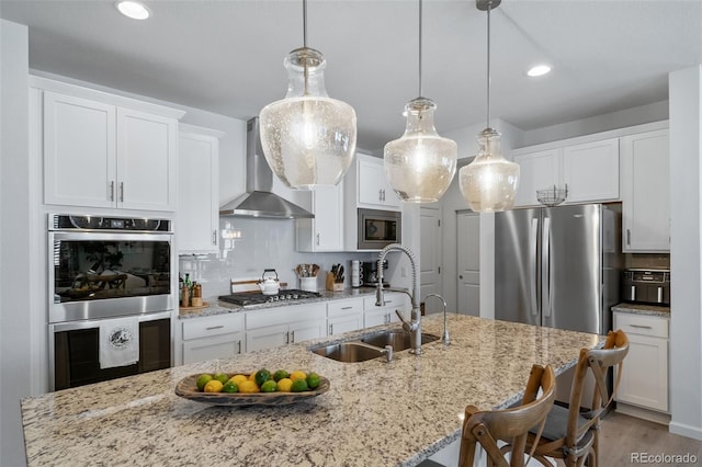 kitchen featuring white cabinets, stainless steel appliances, a sink, and wall chimney range hood