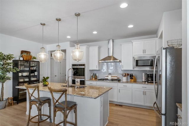 kitchen with white cabinets, a kitchen island with sink, tasteful backsplash, wall chimney range hood, and appliances with stainless steel finishes