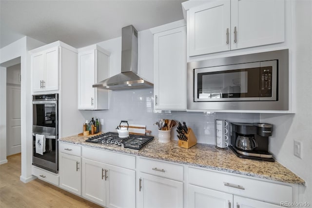 kitchen featuring white cabinets, stainless steel appliances, backsplash, and wall chimney range hood