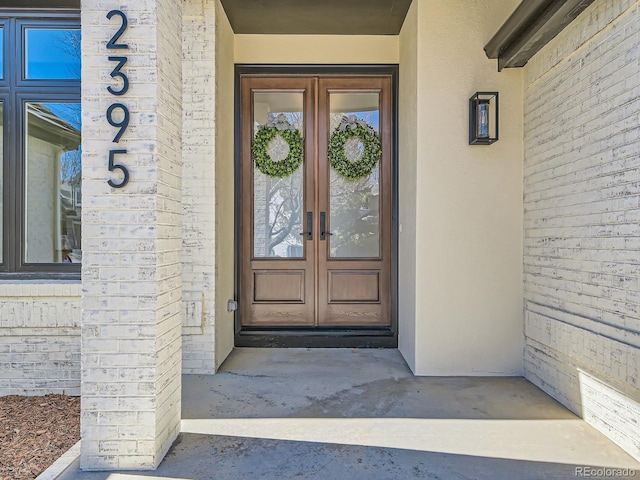 doorway to property featuring french doors, brick siding, and stucco siding