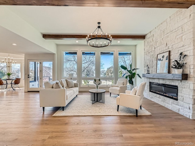 living area with light wood finished floors, a fireplace, beam ceiling, and an inviting chandelier