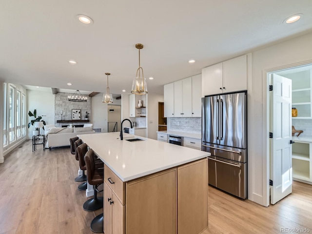 kitchen with light countertops, decorative backsplash, high quality fridge, a sink, and light wood-type flooring