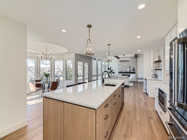 kitchen featuring a notable chandelier, a sink, appliances with stainless steel finishes, backsplash, and light wood finished floors