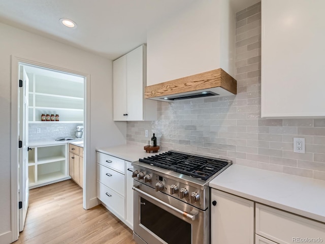 kitchen featuring tasteful backsplash, high end stainless steel range oven, light countertops, light wood-type flooring, and white cabinetry