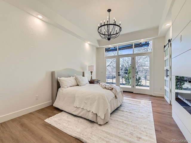 bedroom with a barn door, baseboards, wood finished floors, access to outside, and a chandelier