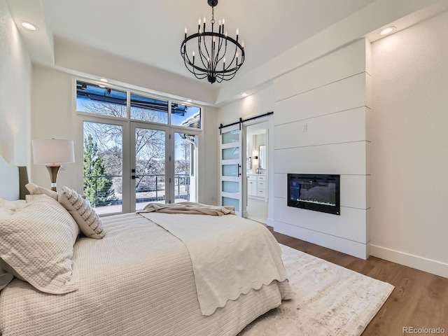 bedroom featuring access to exterior, a barn door, a glass covered fireplace, wood finished floors, and baseboards