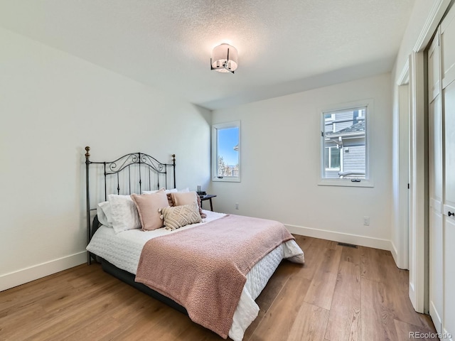 bedroom featuring a closet, baseboards, a textured ceiling, and light wood finished floors