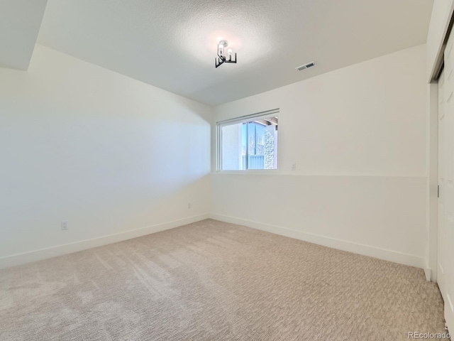 empty room with light colored carpet, visible vents, a textured ceiling, and baseboards