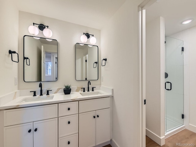 bathroom featuring baseboards, double vanity, a sink, and a shower stall