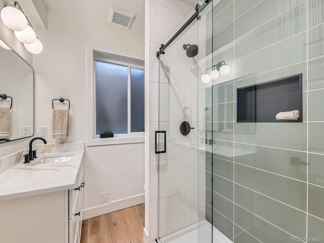 bathroom with wood finished floors, vanity, visible vents, baseboards, and a shower stall