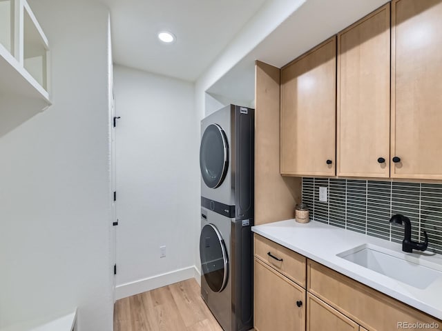 washroom featuring stacked washer / dryer, a sink, baseboards, cabinet space, and light wood finished floors