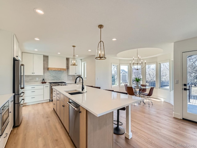 kitchen featuring premium appliances, custom exhaust hood, light wood-style flooring, a sink, and a chandelier