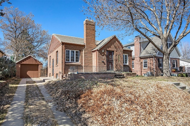 view of front of house featuring a tile roof, concrete driveway, an outdoor structure, brick siding, and a chimney