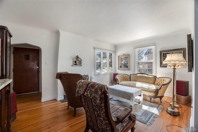 living room featuring arched walkways, light wood-type flooring, and baseboards