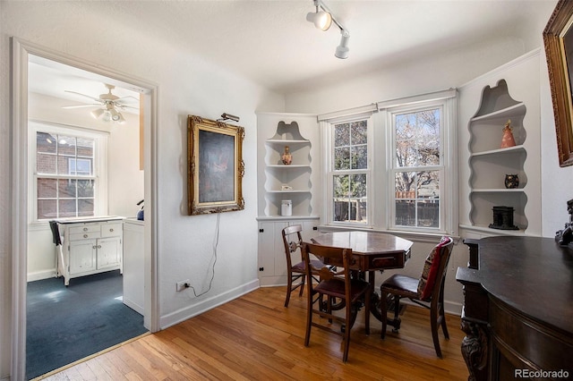 dining space with dark wood-style floors, track lighting, a ceiling fan, and baseboards