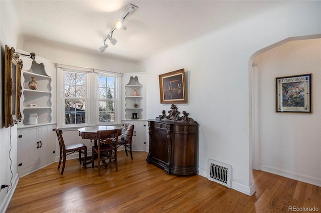 dining area with visible vents, light wood-style flooring, track lighting, arched walkways, and baseboards