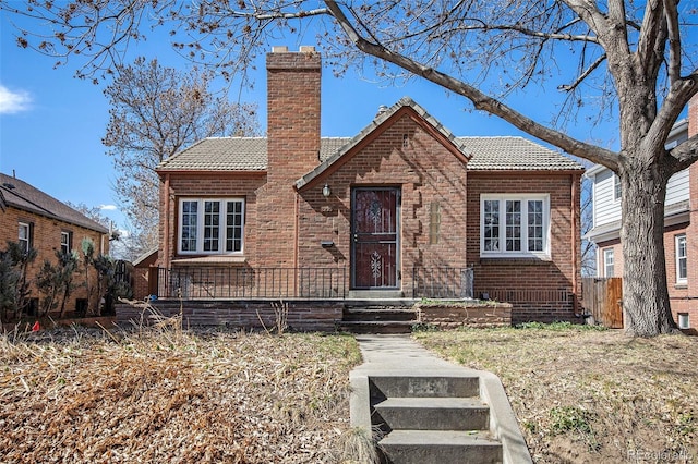 view of front facade featuring brick siding, a tiled roof, and a chimney