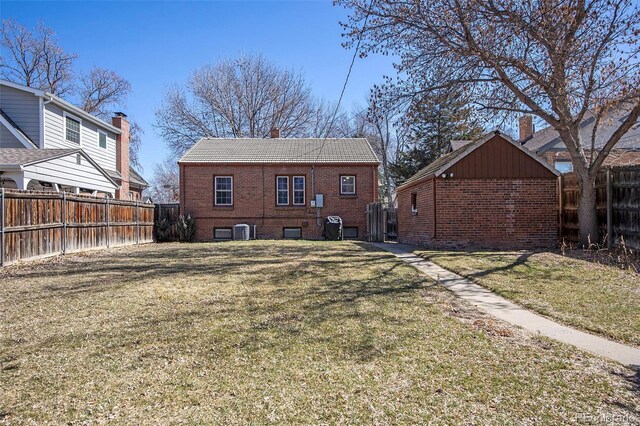 back of house with a lawn, a fenced backyard, brick siding, and an outdoor structure