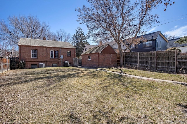 rear view of house featuring a lawn, central AC, a fenced backyard, brick siding, and a chimney