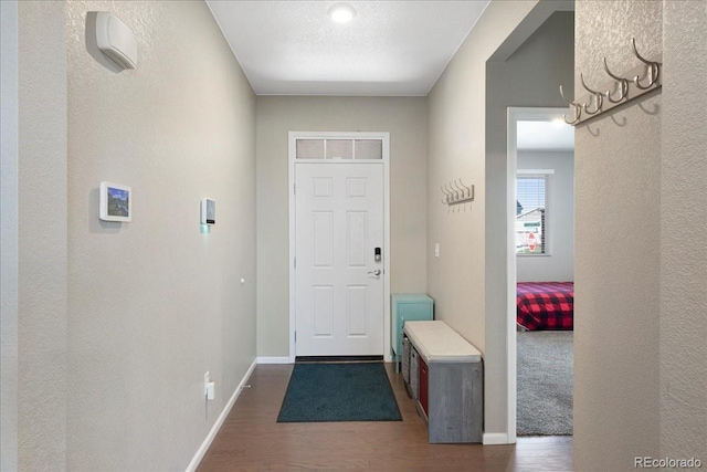 entryway featuring baseboards, a textured wall, and dark wood-type flooring