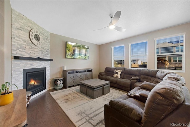 living area with light wood-type flooring, a ceiling fan, and a stone fireplace