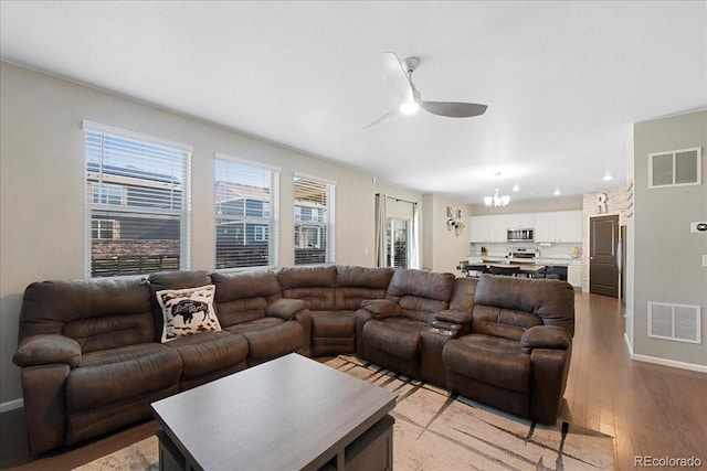 living area featuring light wood-style floors, baseboards, ceiling fan with notable chandelier, and visible vents