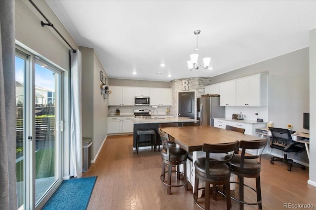 kitchen with dark wood-style flooring, appliances with stainless steel finishes, a chandelier, and a center island with sink