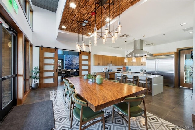dining room featuring visible vents, a barn door, a high ceiling, and a chandelier
