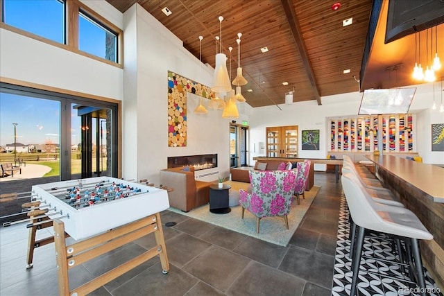 playroom featuring a glass covered fireplace, a towering ceiling, a wealth of natural light, and wooden ceiling