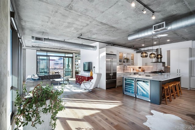 kitchen with high end fridge, wall chimney range hood, pendant lighting, a center island, and white cabinetry