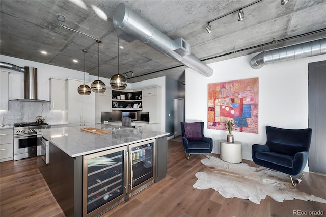 kitchen with pendant lighting, stainless steel stove, beverage cooler, and wall chimney exhaust hood