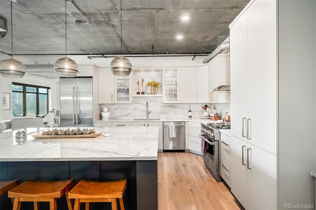 kitchen featuring pendant lighting, a breakfast bar, high quality appliances, light stone countertops, and white cabinetry